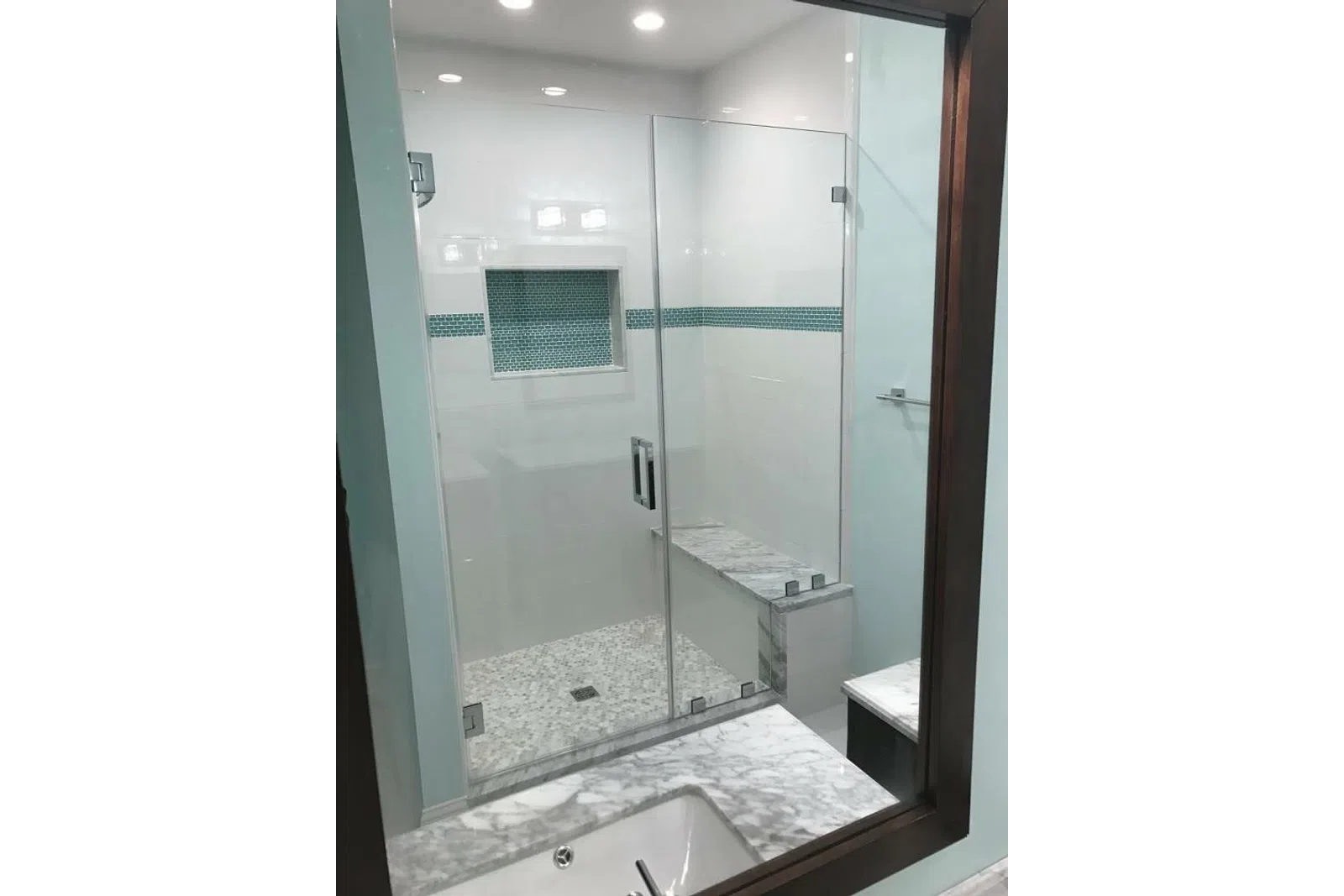 Modern bathroom shower with glass doors, marble bench, mosaic tile niche, and light blue accents.