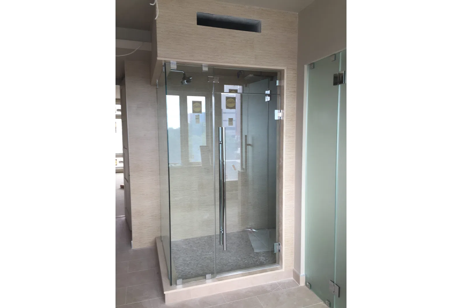 Modern glass shower enclosure with chrome handle and beige tiled walls and floor in a bright bathroom