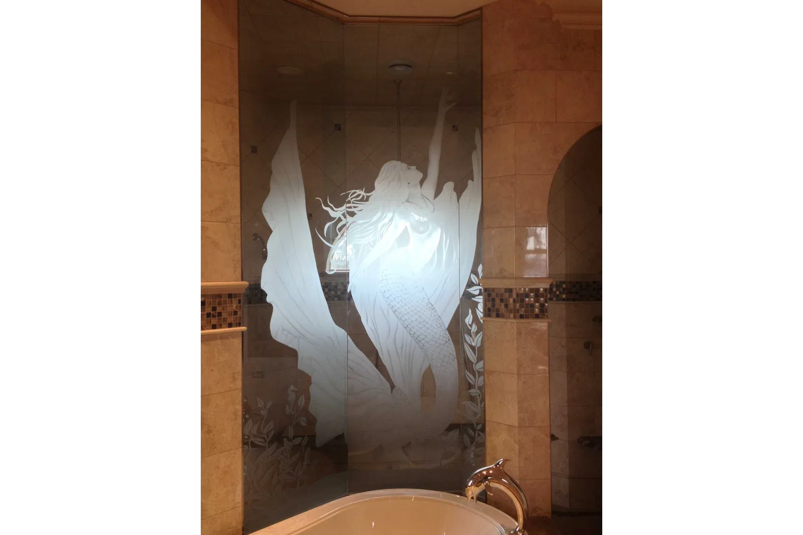 Etched glass shower door with a detailed mermaid design in a beige tiled bathroom near a bathtub.