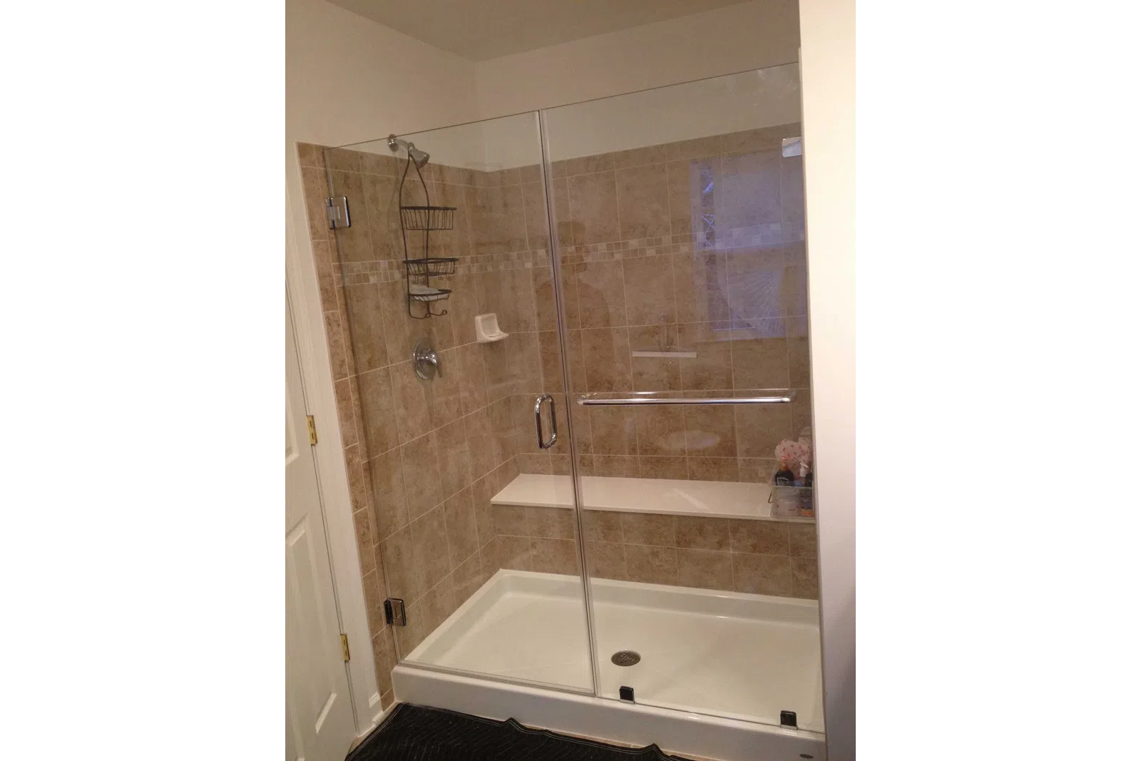 Glass shower enclosure with beige tile walls, built-in bench, showerhead, and metal shower caddy.
