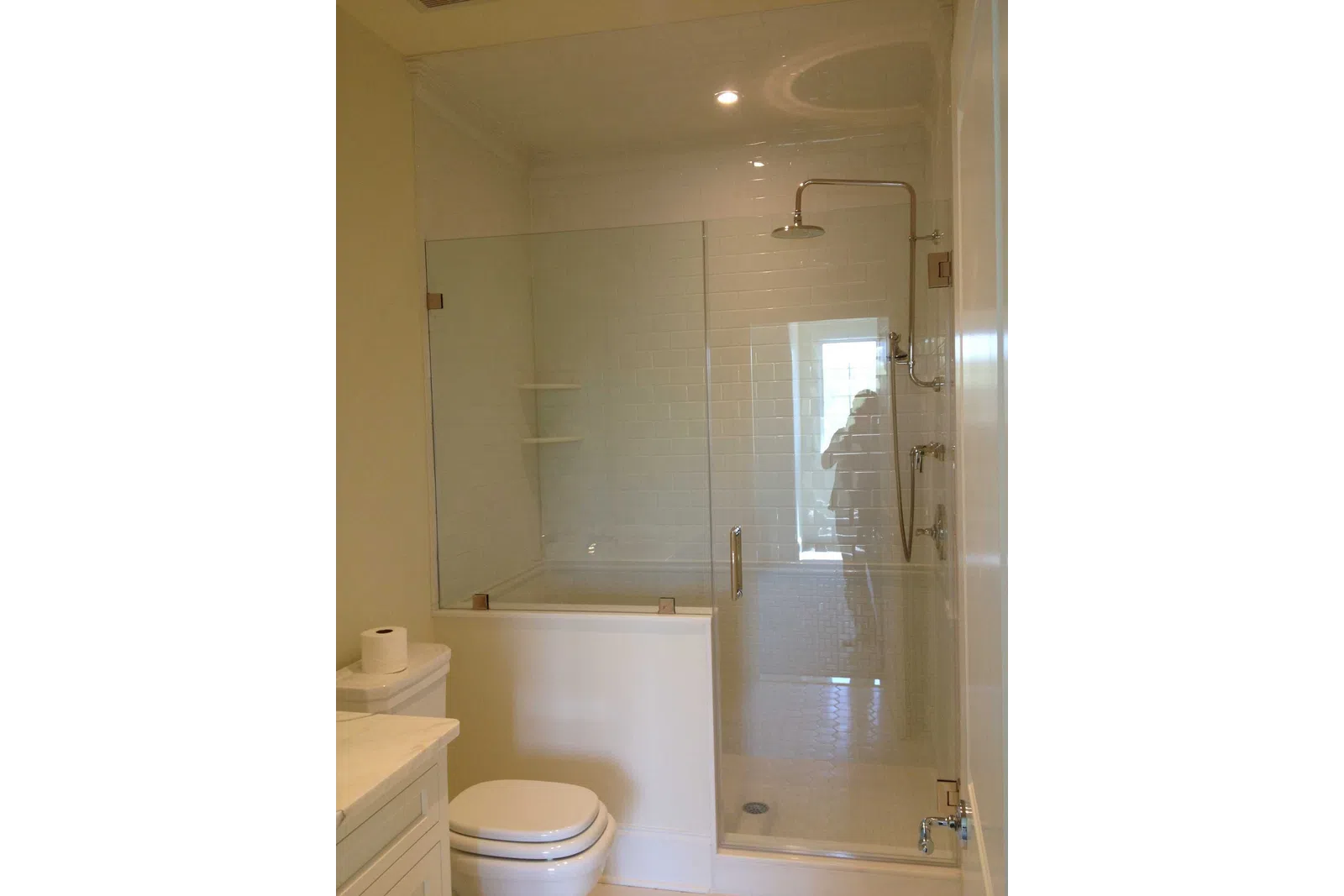 Modern bathroom with glass-enclosed shower, white subway tiles, toilet, and marble countertop vanity.