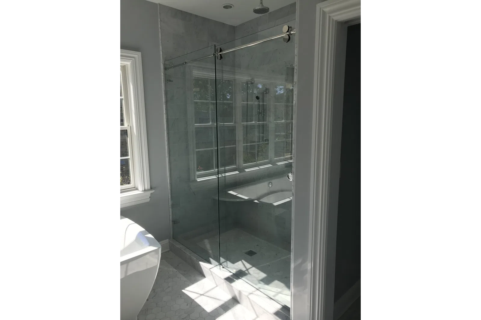 Modern bathroom featuring a glass-enclosed shower with marble tiles and natural light from a nearby window.