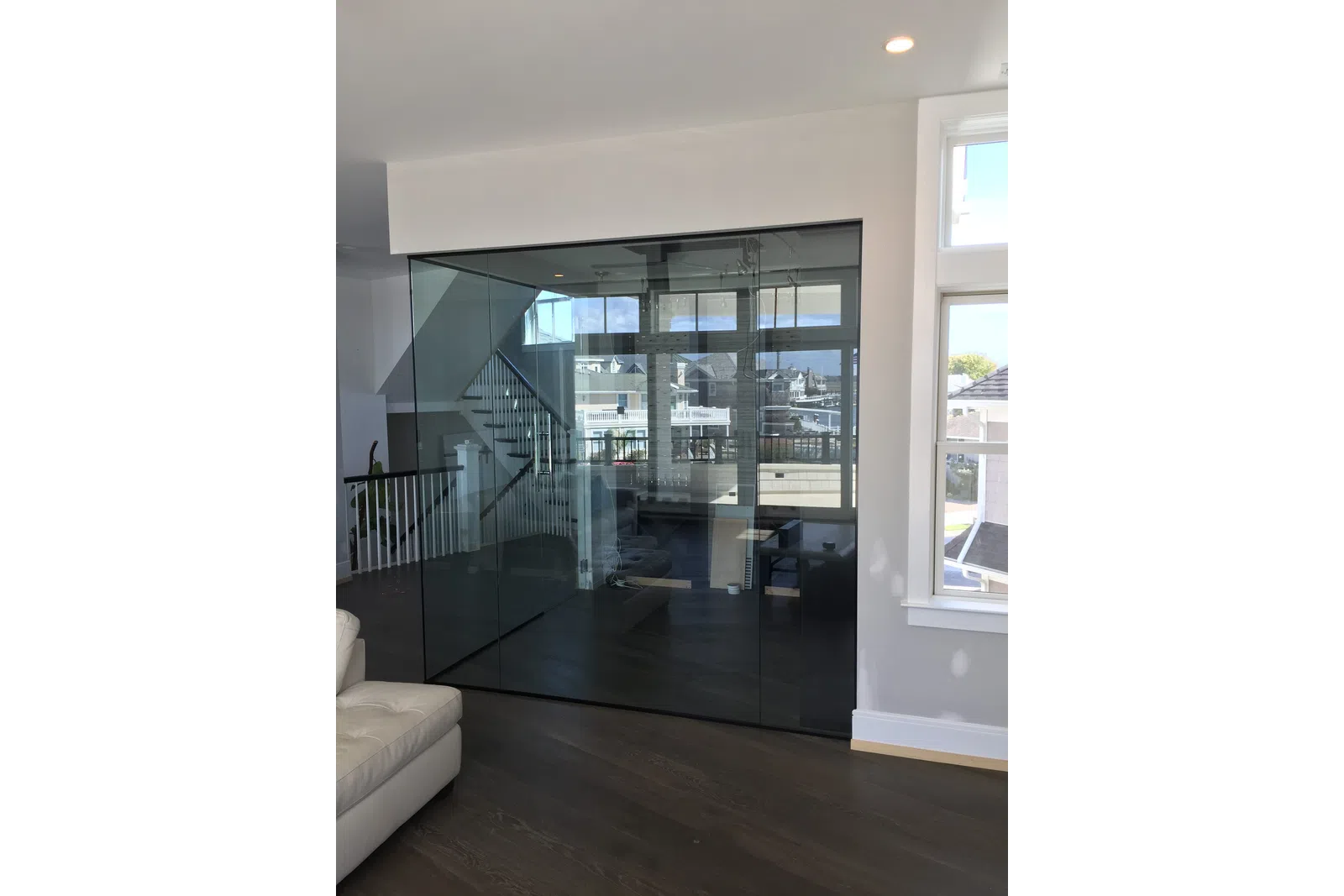Modern interior with glass wall partition separating living space and staircase, featuring dark wood floors and white furniture.