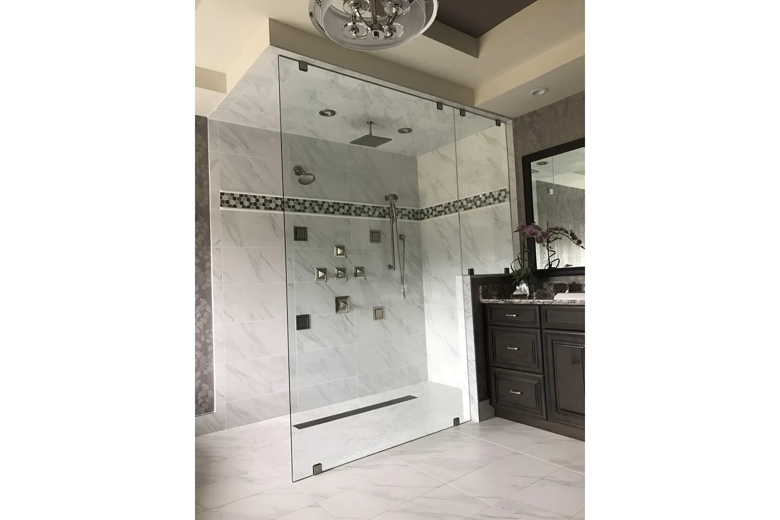 Modern bathroom with a glass-enclosed marble shower, rainfall showerhead, dark wood vanity, and large mirror.