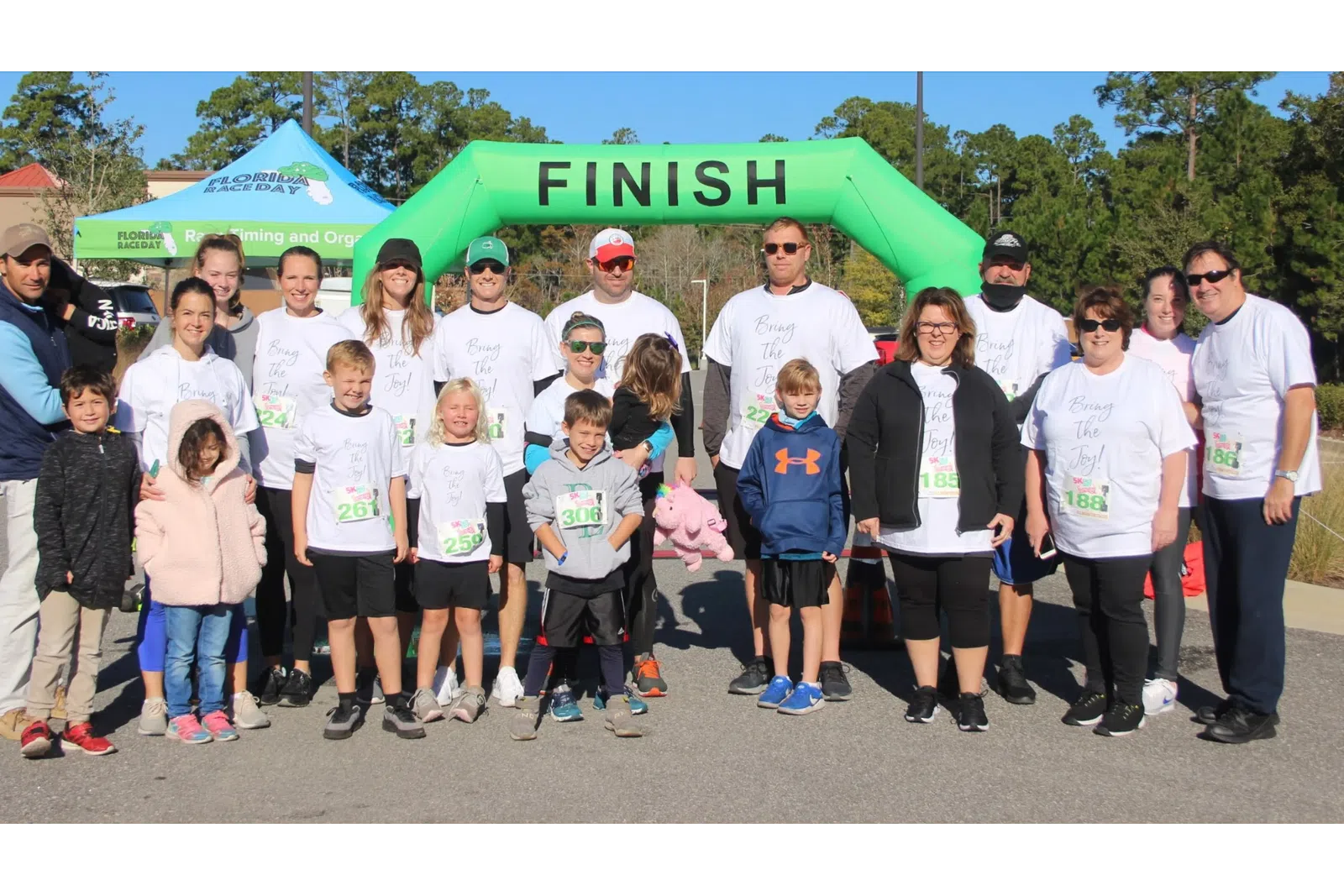 Group of adults and children in matching shirts standing together at a race finish line outdoors