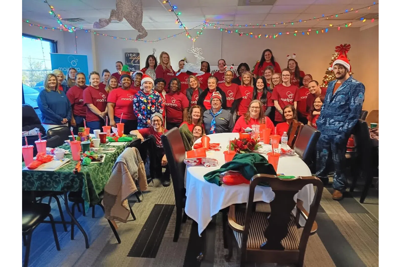 Large group of people in red shirts celebrating Christmas with festive decorations and lights indoors
