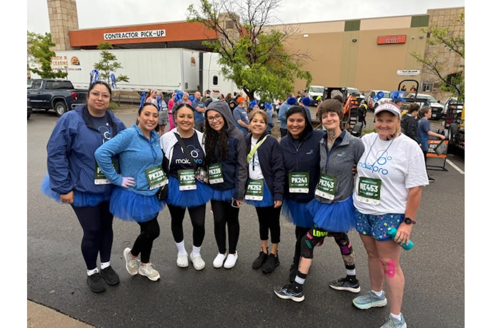 Group of women in blue tutus and race bibs posing together outdoors before a race or charity run event.