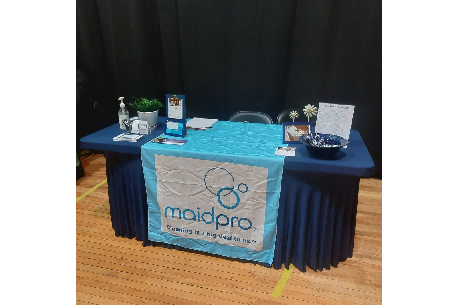 MaidPro promotional table with cleaning products, brochures, and branded table cover at an indoor event.