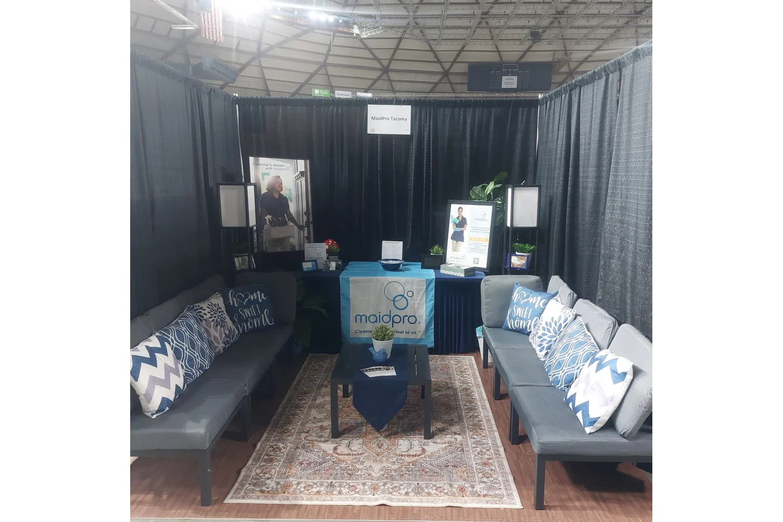 MaidPro Tacoma booth with couches, pillows, table, plants, and promotional banners at an event