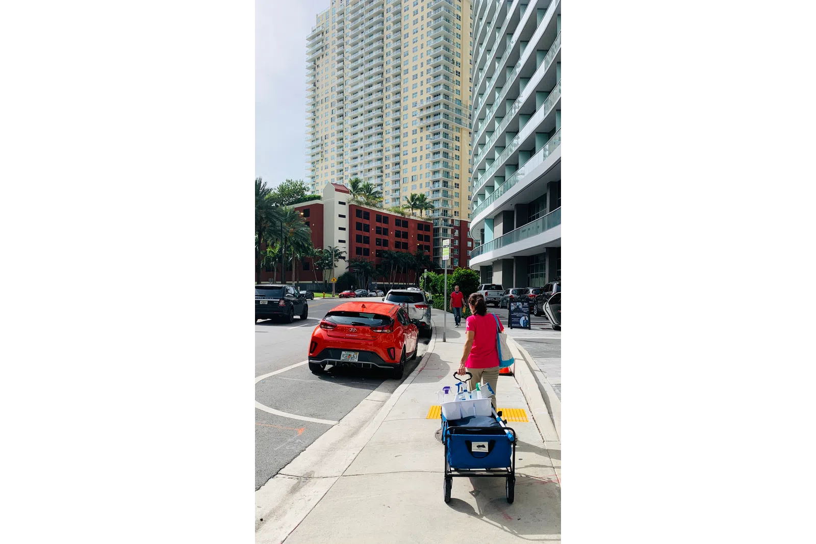 a person pushing a cart on a sidewalk next to a street with cars and buildings