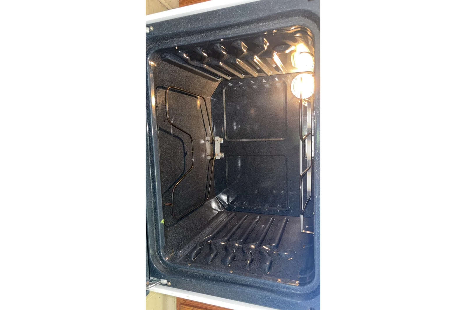 Empty clean kitchen oven interior with heating elements and bright interior light on right side
