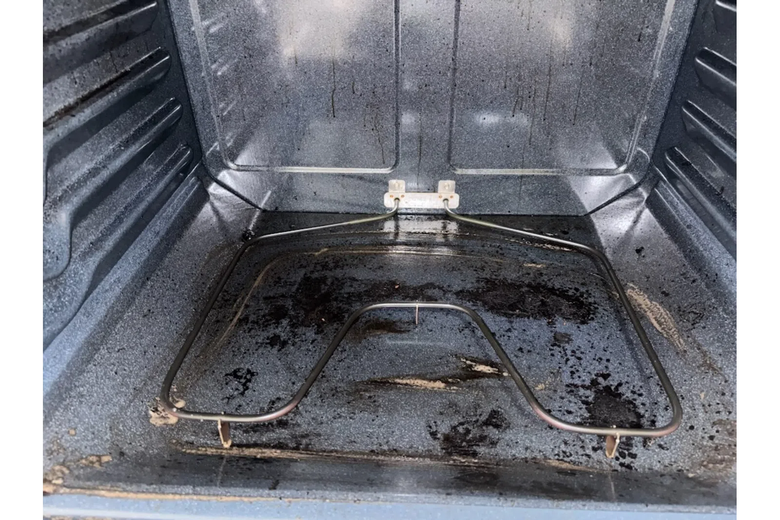 Close-up of a dirty oven interior with burnt residue and heating element at the bottom.