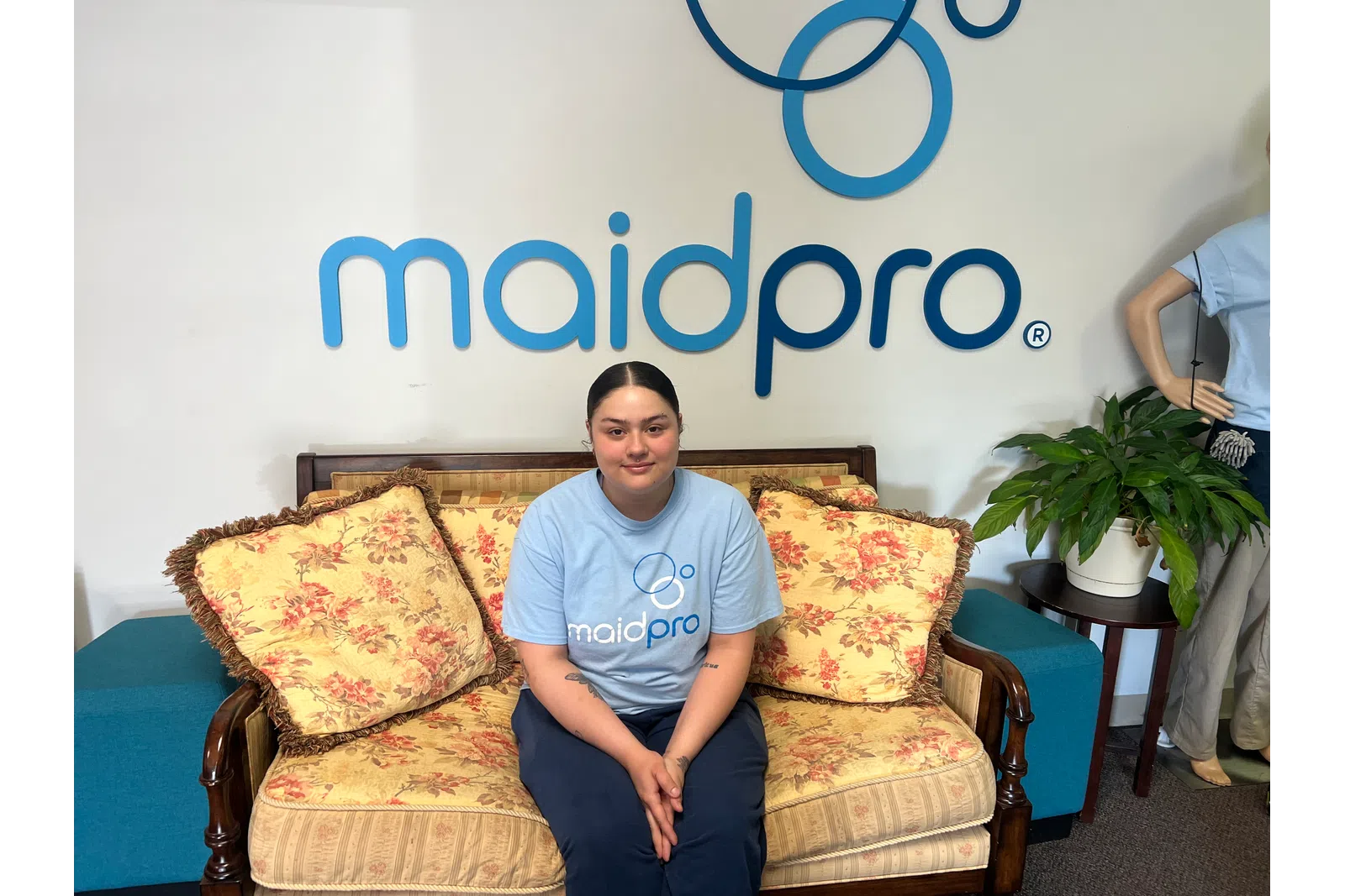 MaidPro employee sitting on floral couch under MaidPro logo in a clean, welcoming office space.