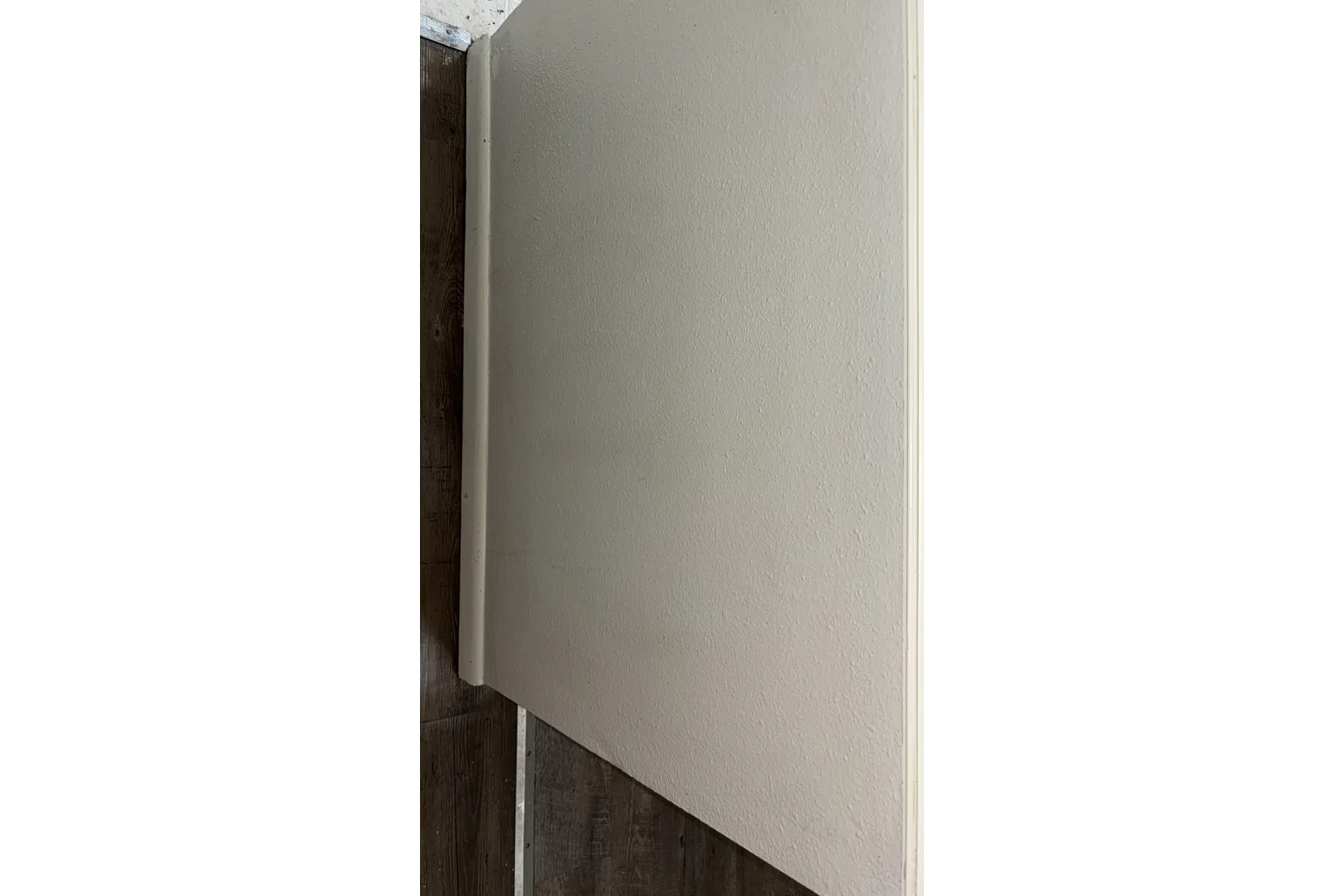 Close-up of a beige textured wall meeting dark wood flooring with white baseboard trim.