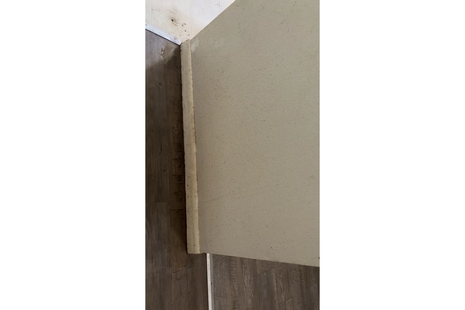 Close-up of textured beige wall corner meeting dark wooden floor with visible grout and baseboard.