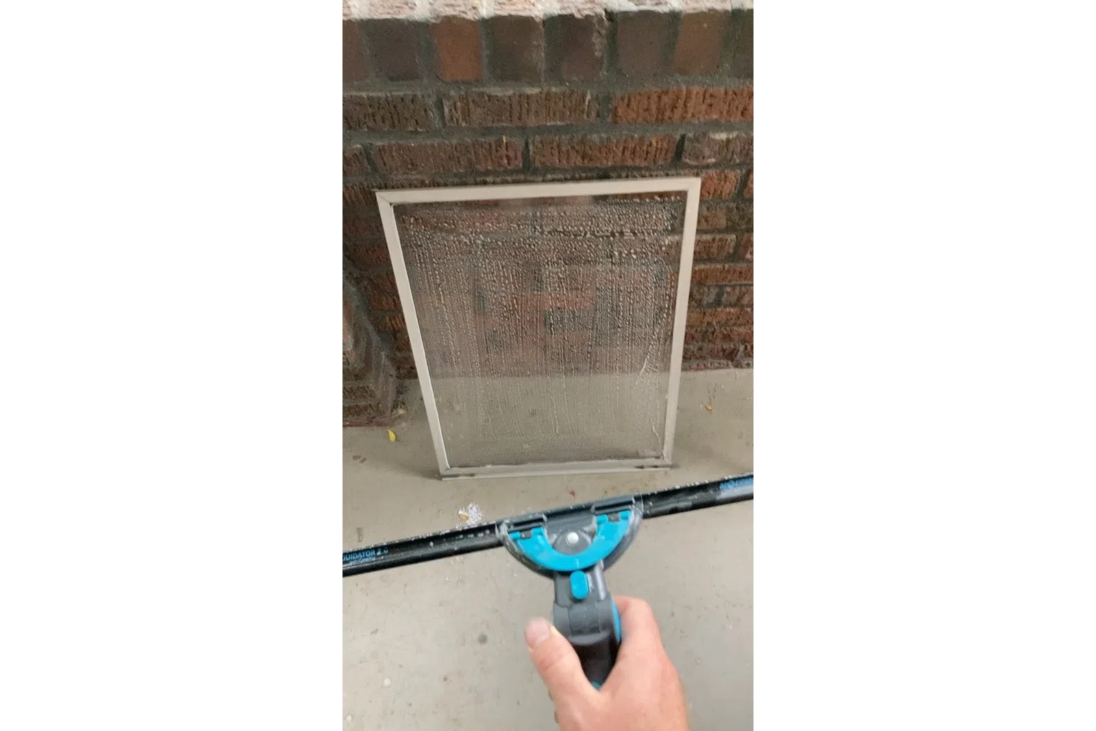 a hand holding a blue and black object in front of a brick wall