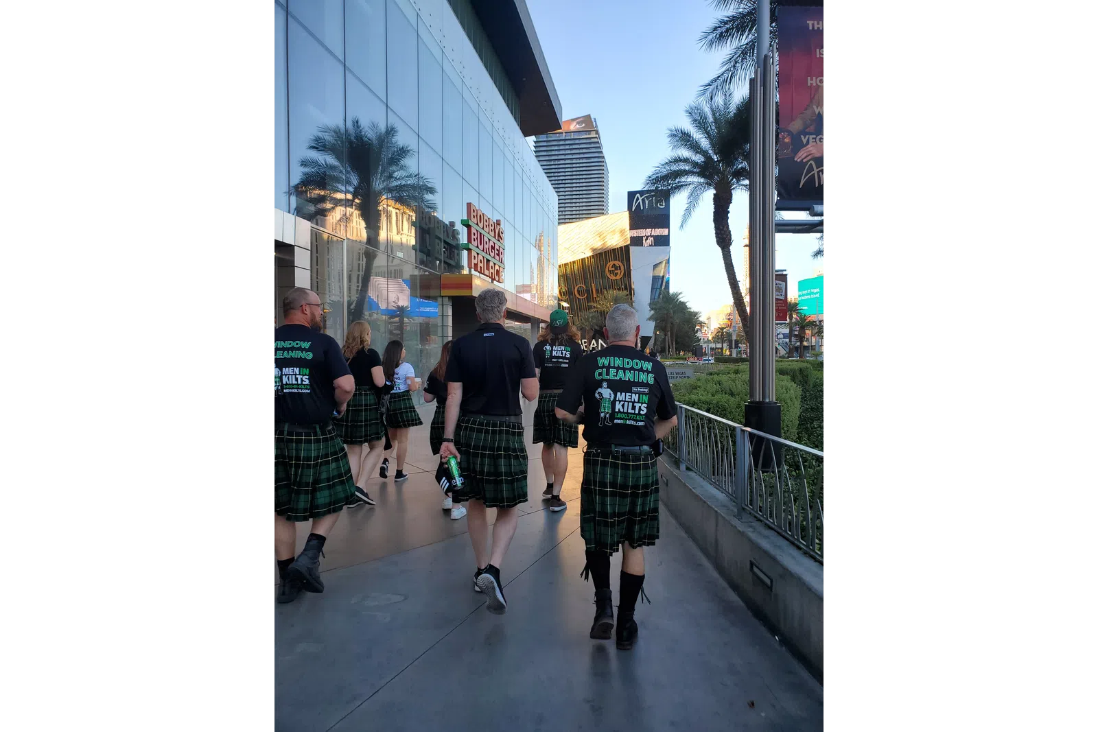 Group of people wearing kilts and Men in Kilts window cleaning shirts walking on a sunny city sidewalk in Las Vegas.