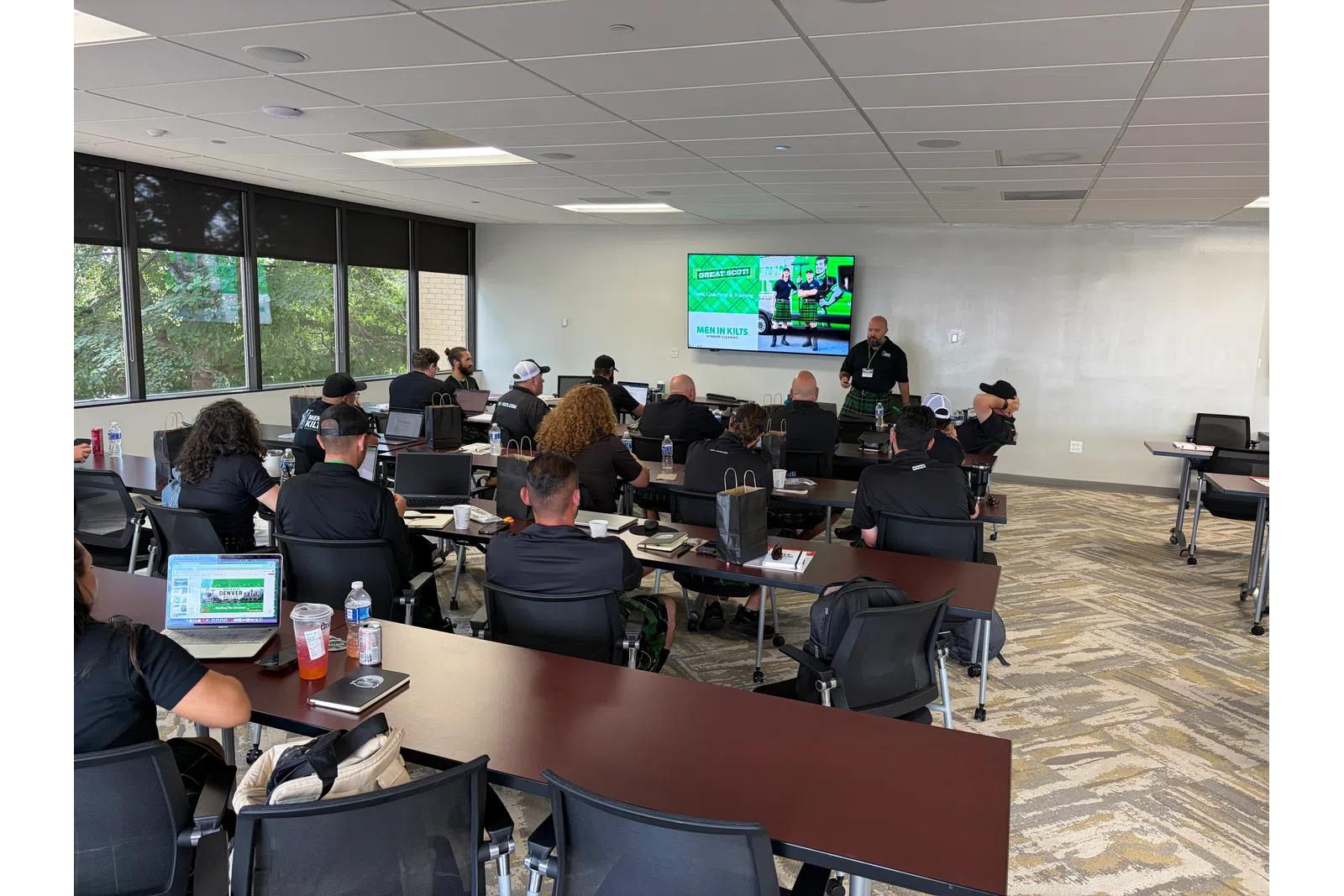 Instructor giving a presentation to adult students in a modern classroom with laptops and notebooks