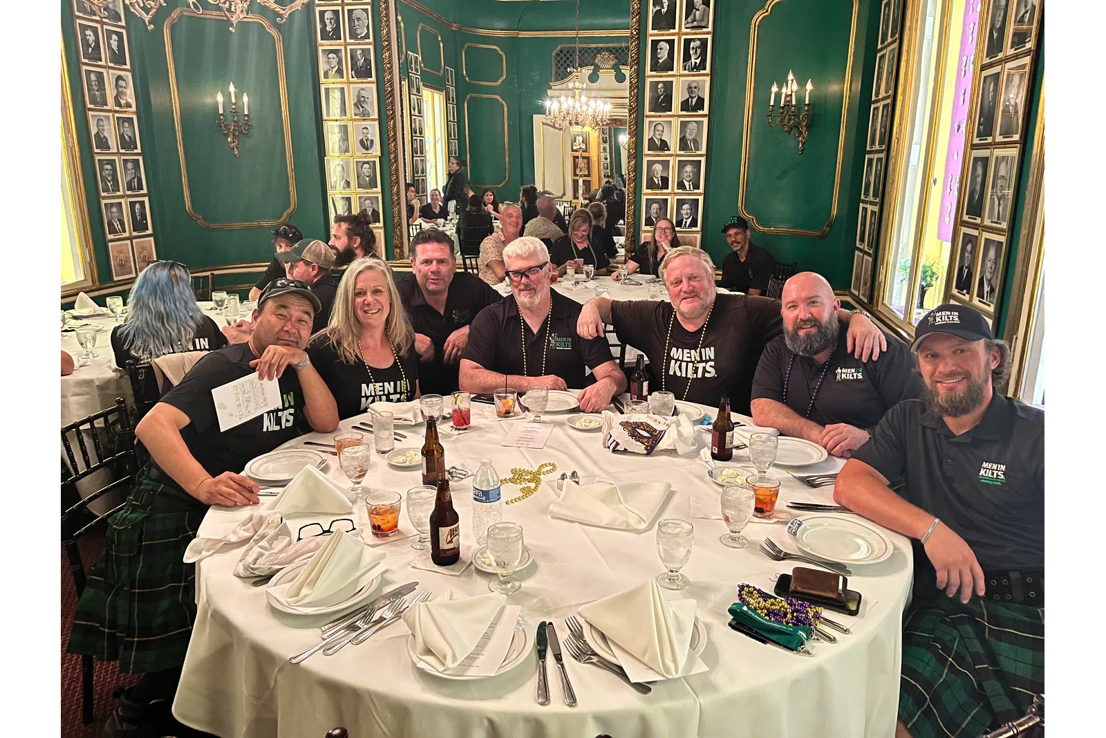 Group of men and women wearing kilts seated around a table in an ornate green and gold dining room.