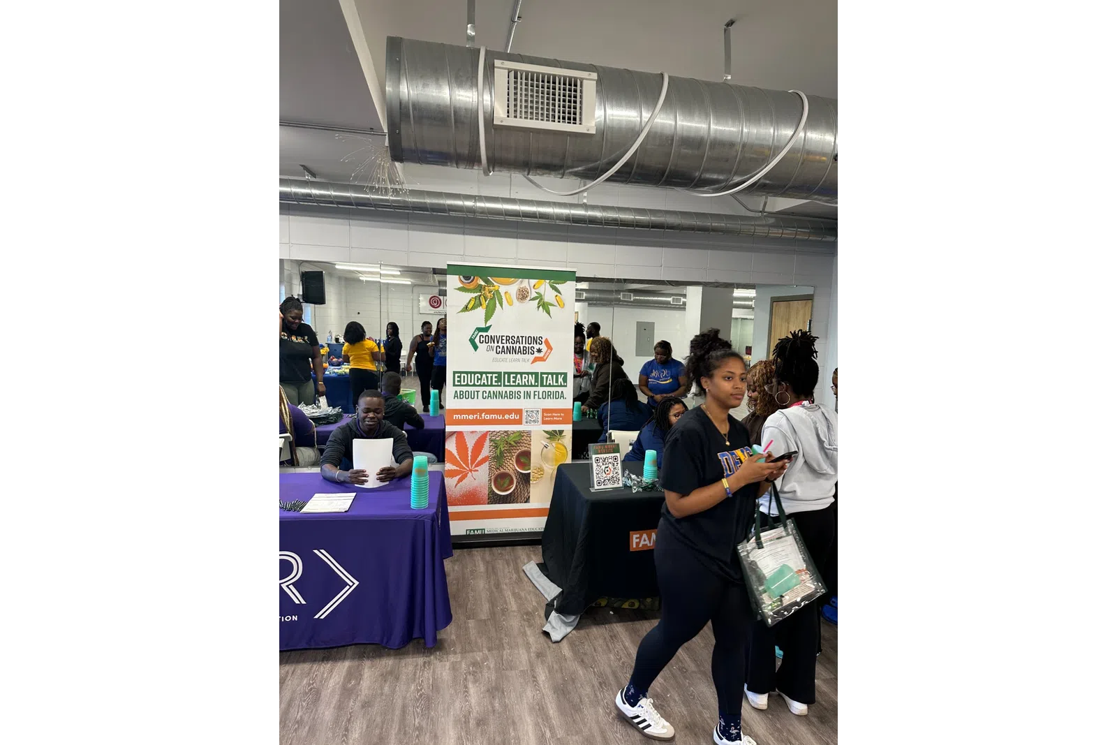 People attending an educational cannabis event with informational tables and promotional banners indoors.