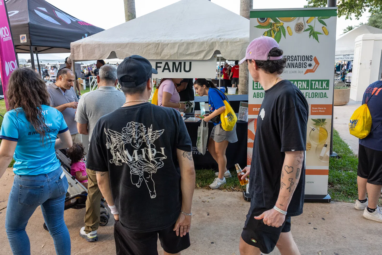 People gather near FAMU booth at an outdoor event with informational banners and tents under daylight.