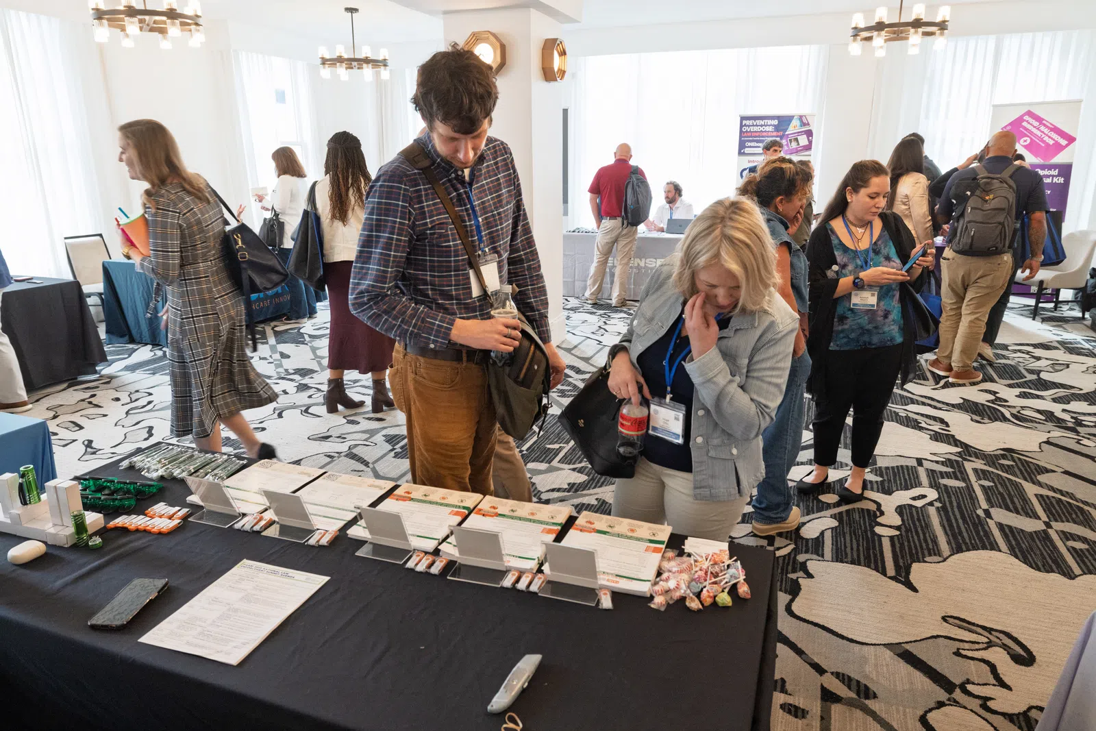 People browsing informational booths at a professional networking event in a bright conference room.