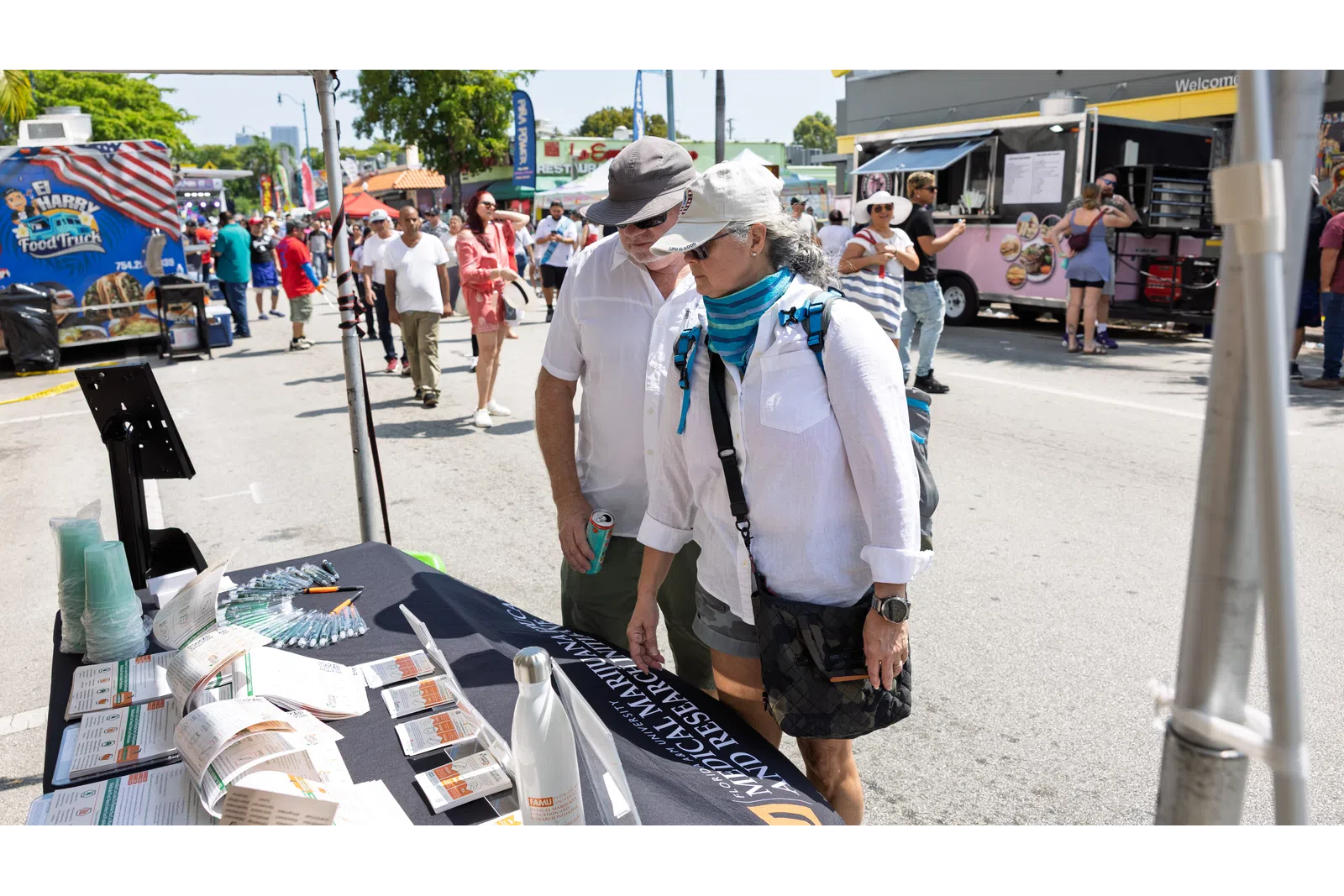 Couple browsing informational booth at outdoor festival with food trucks and crowd in the background