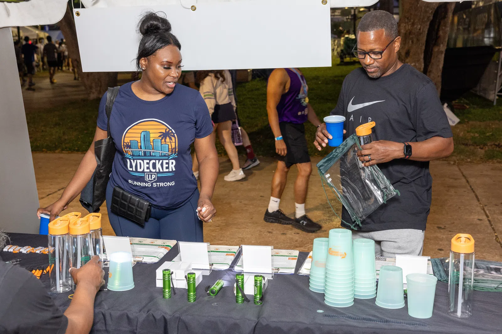 Two people at an outdoor booth with promotional water bottles and cups during a nighttime event