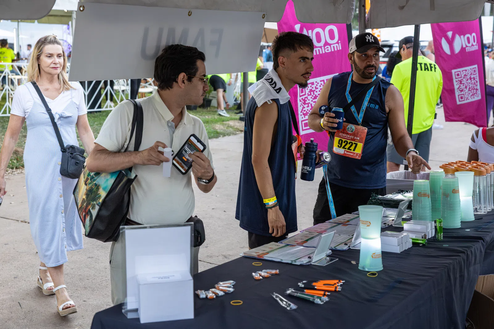 People interacting at an outdoor booth with promotional items and banners at an event under a tent.