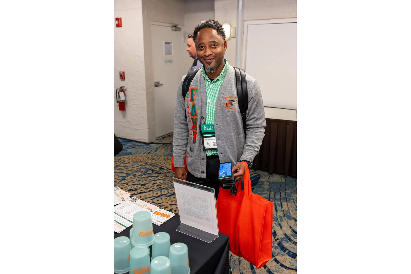 a man wearing a backpack and lanyard standing next to a table with a bottle of water