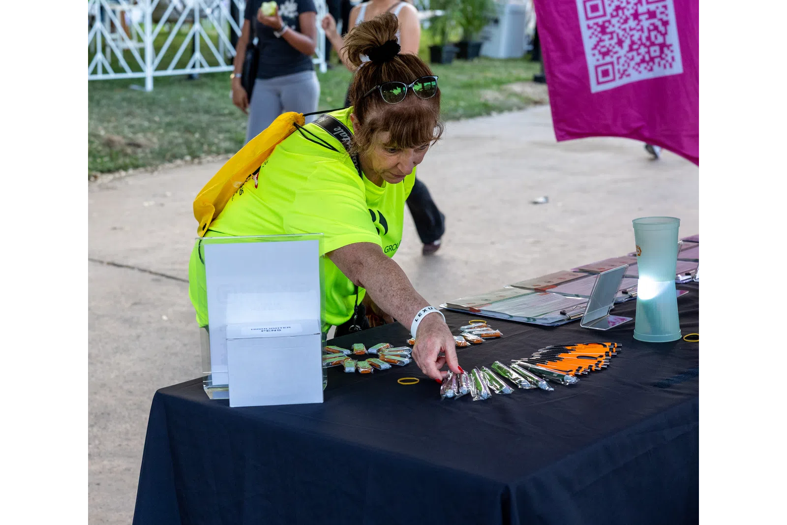 Woman in neon yellow shirt arranging promotional items on a black table at an outdoor event.