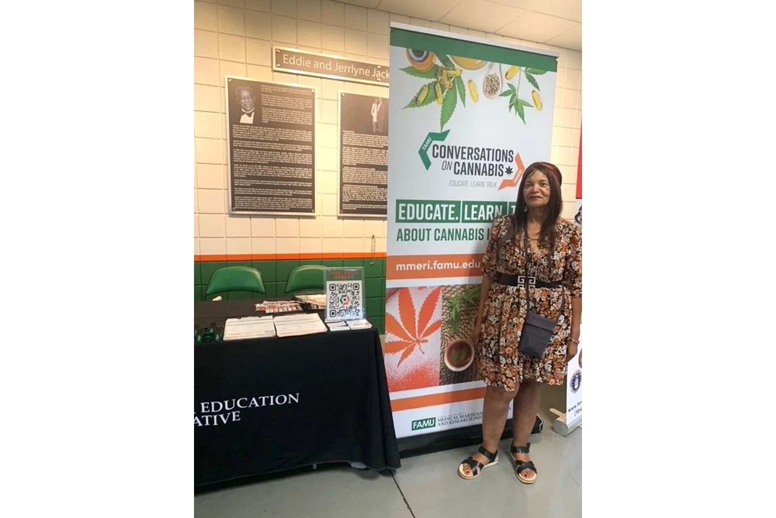 Woman standing next to a cannabis education booth with informational banner and brochures in a public space.