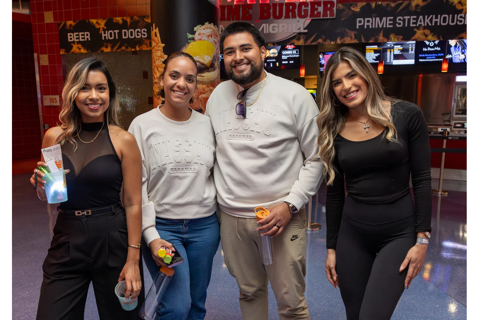 Four friends smiling at a restaurant counter with menu screens featuring burgers, hot dogs, and beer in the background.