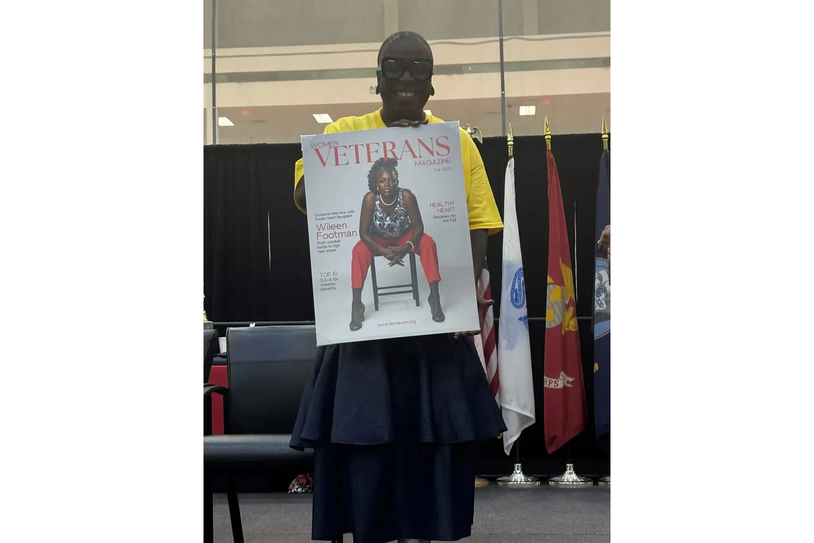 Person holding a Women Veterans Magazine cover featuring a seated woman in red pants and patterned top.