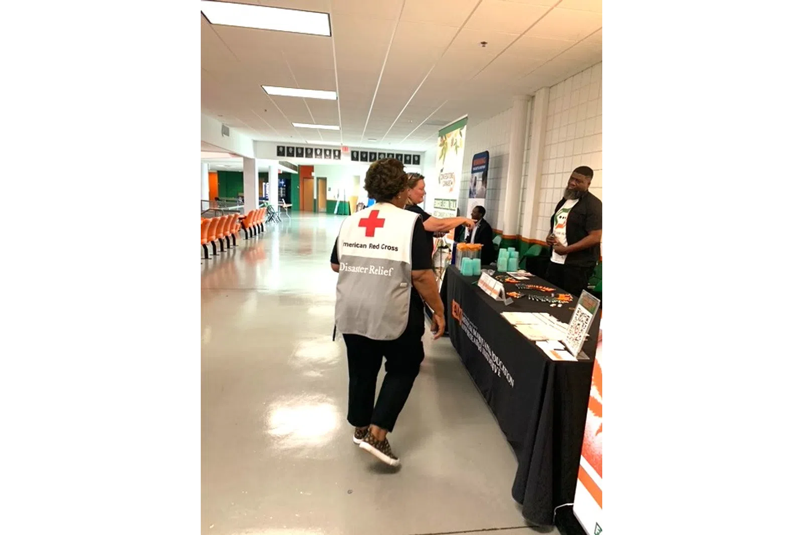 American Red Cross Disaster Relief volunteer walking towards an information booth in a large indoor space.