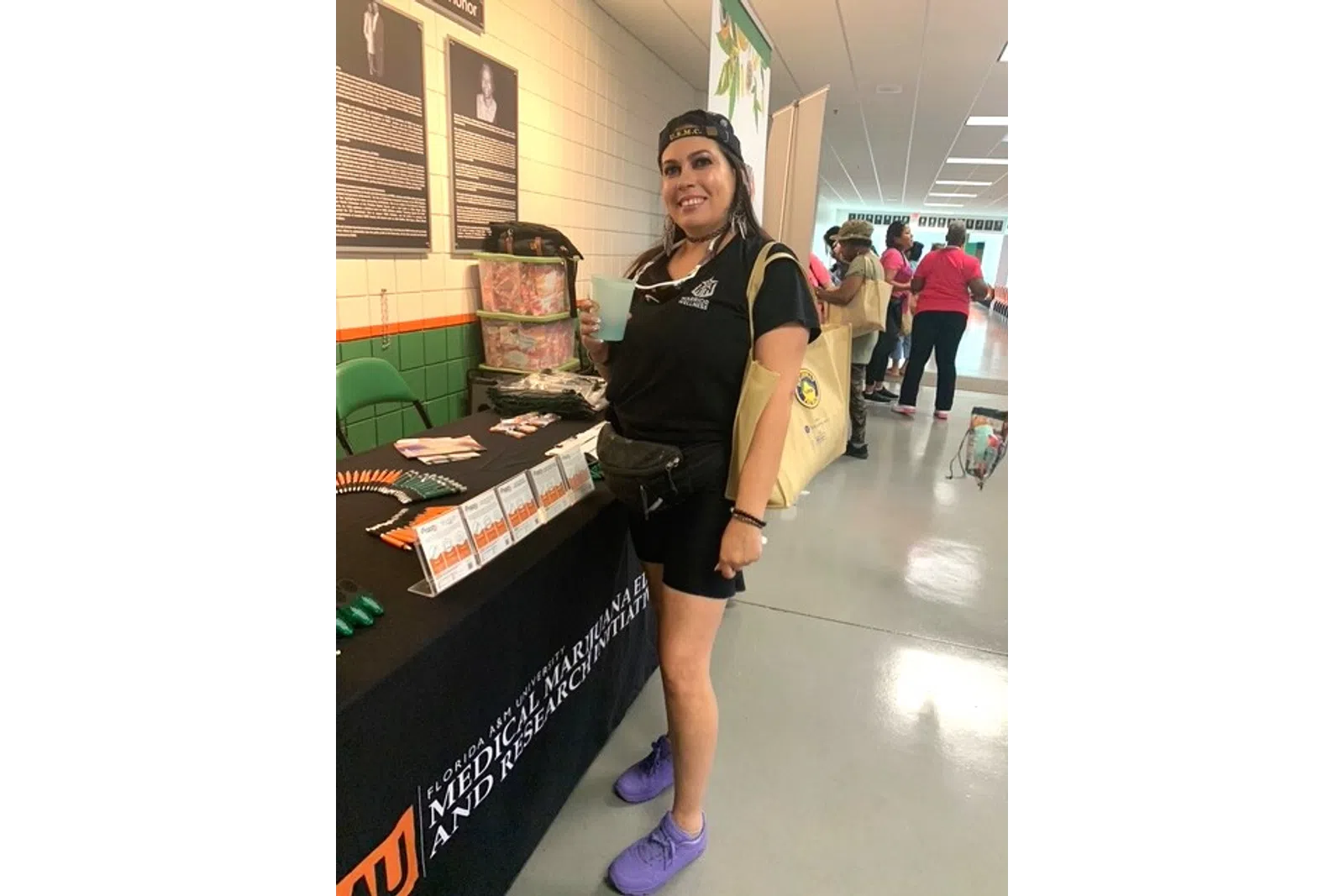 Smiling woman in black outfit holding drink at a Florida A&M University Medical Marijuana research booth.