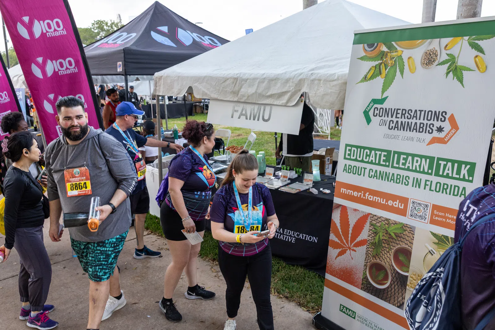 People at an outdoor event near a tent promoting cannabis education by FAMU in Florida with banners and pamphlets.