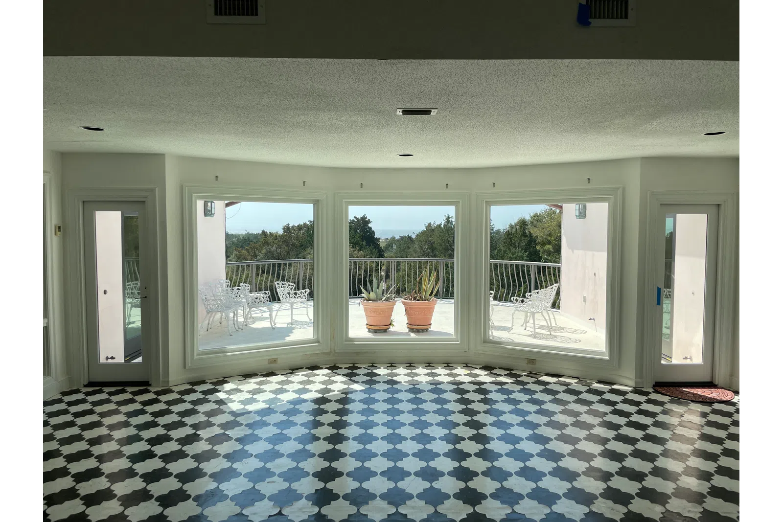 Bright room with black and white patterned floor, large windows, and a balcony with chairs and plants