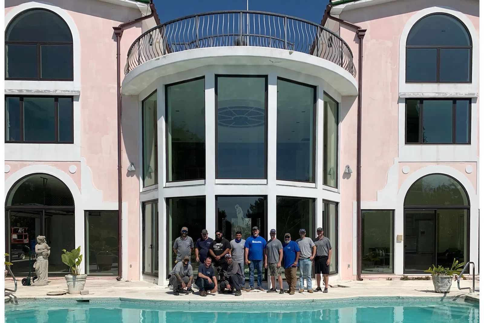Group of people posing by a large modern house with tall windows and a swimming pool in front.