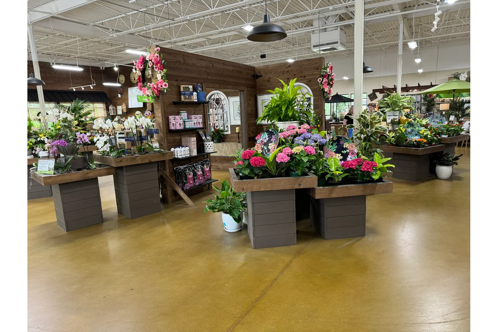 Indoor garden center with wooden planters displaying colorful flowers and green plants under bright lighting.