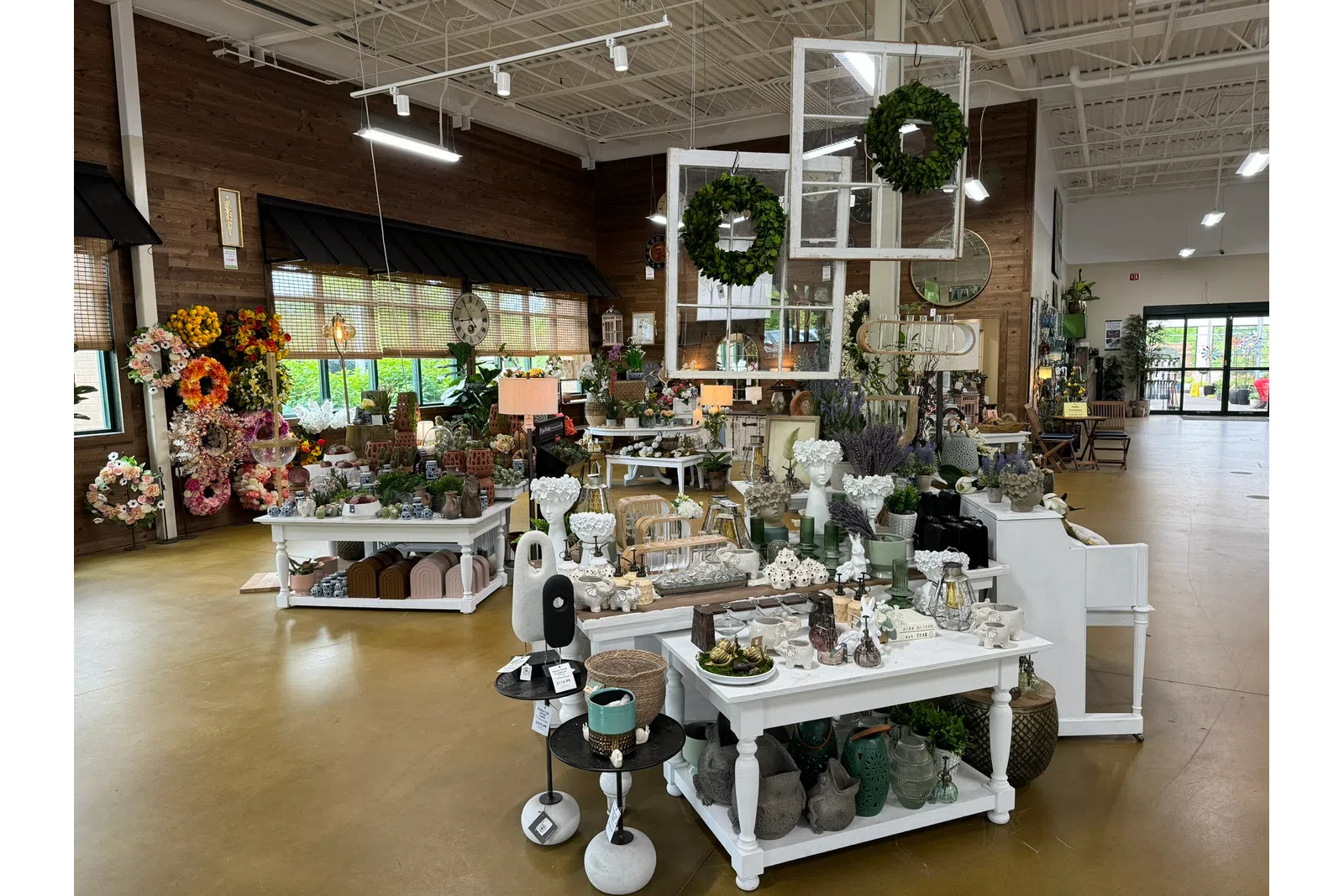 Interior of a bright home decor store displaying floral wreaths, vases, sculptures, and decorative items on tables.
