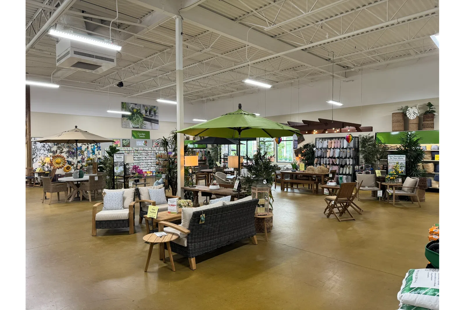 Indoor garden center showroom with outdoor furniture, umbrellas, plants, and home decor displays under bright lighting.