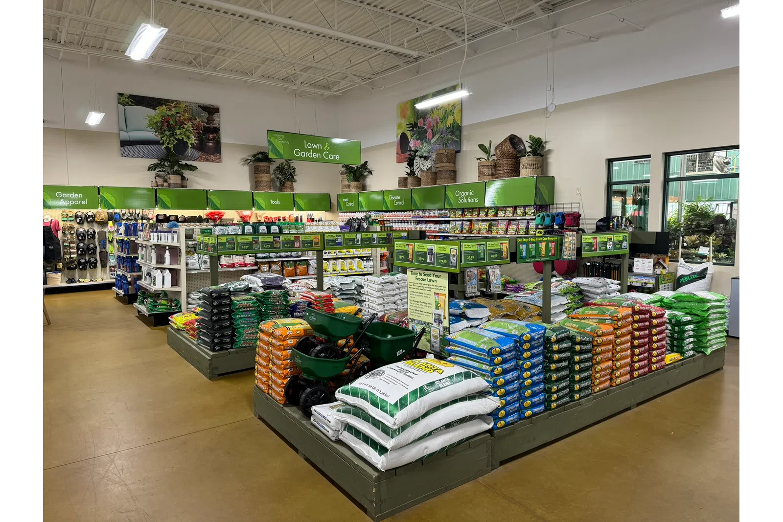 Interior of a garden center with organized shelves of lawn care products, fertilizers, tools, and garden supplies.