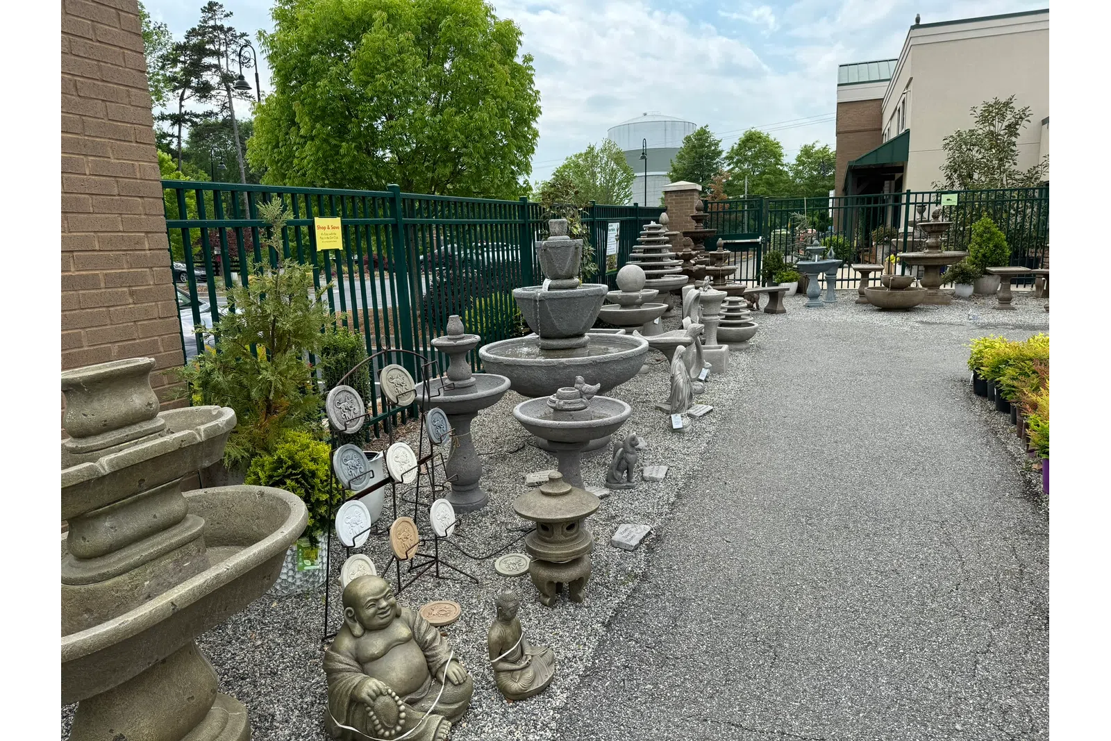 Outdoor garden center display featuring stone fountains, statues, and decorative ornaments on gravel and pavement.