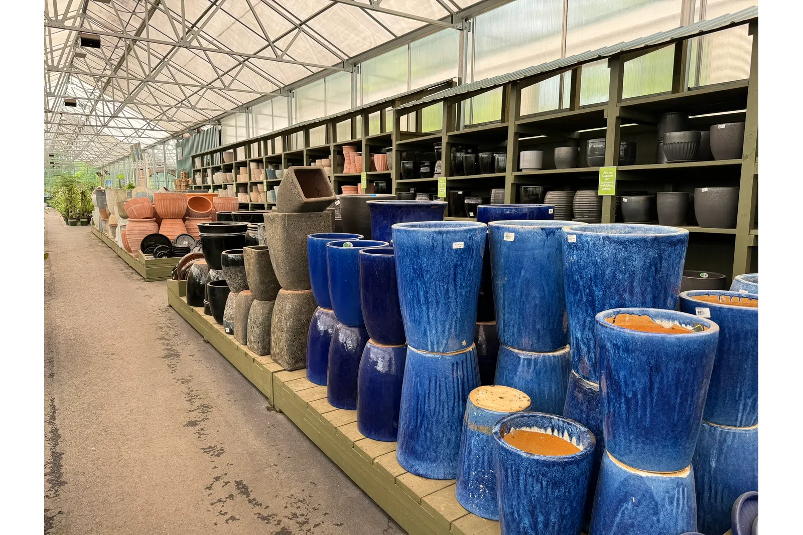Rows of various ceramic and pottery plant pots in different shapes and colors displayed in a garden center aisle.