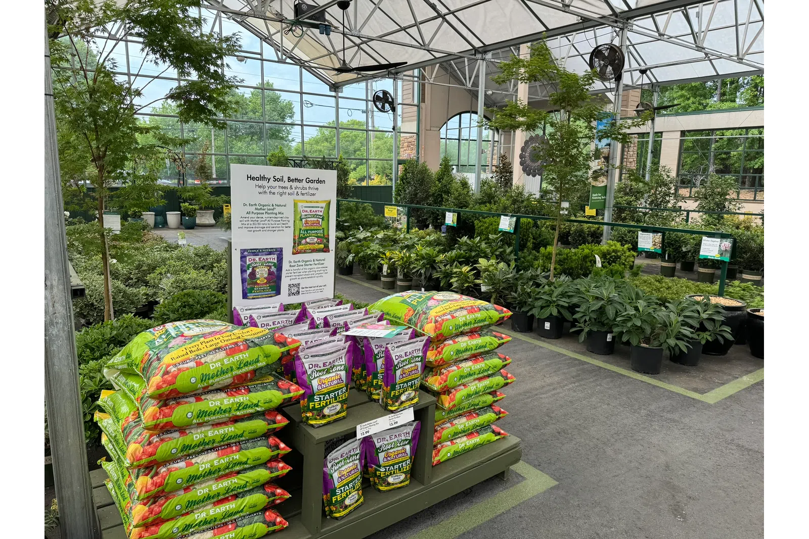 Bags of Dr. Earth soil and fertilizer displayed in a greenhouse with plants and trees in the background.