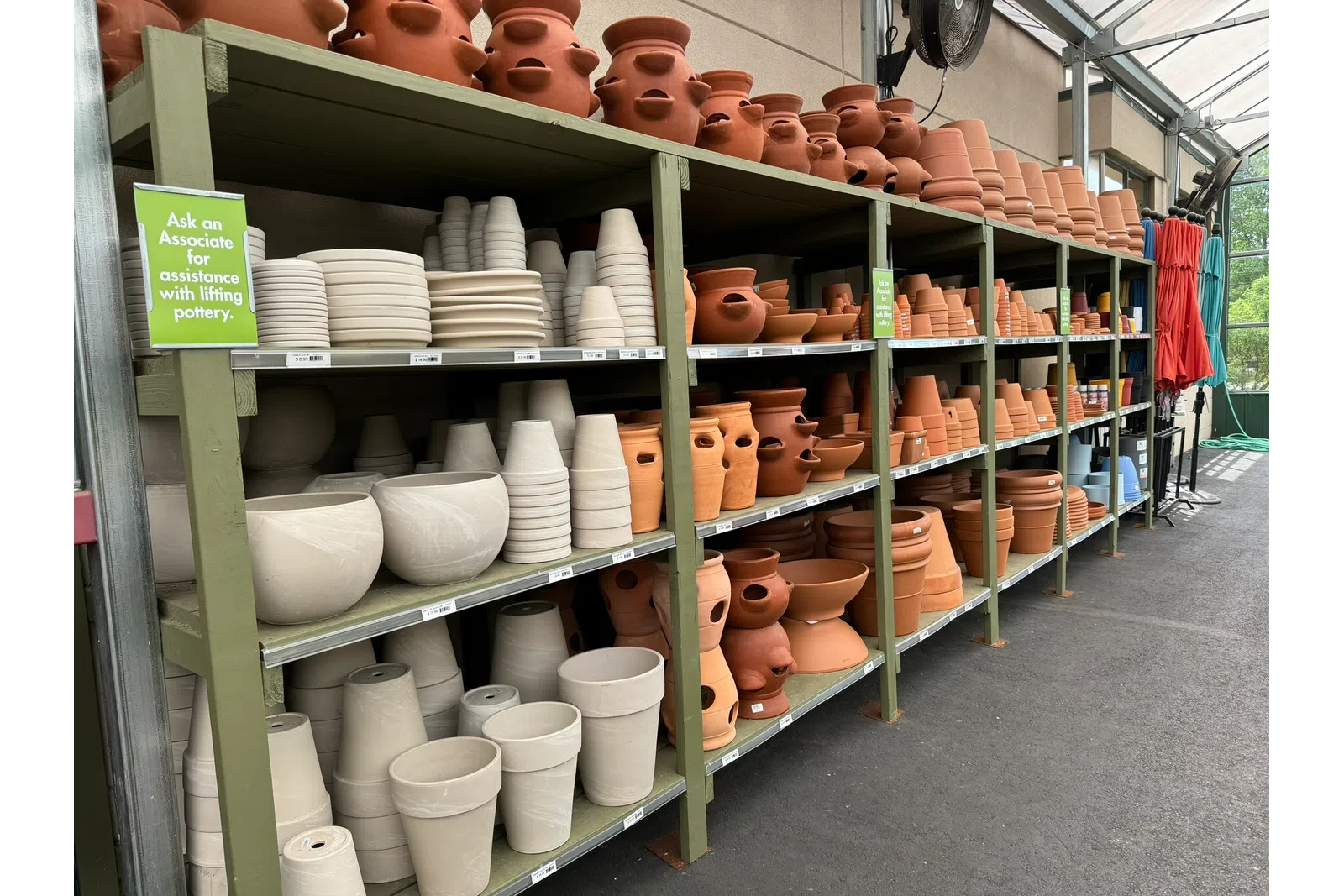 Shelves filled with various terra cotta and ceramic flower pots in a greenhouse nursery aisle.