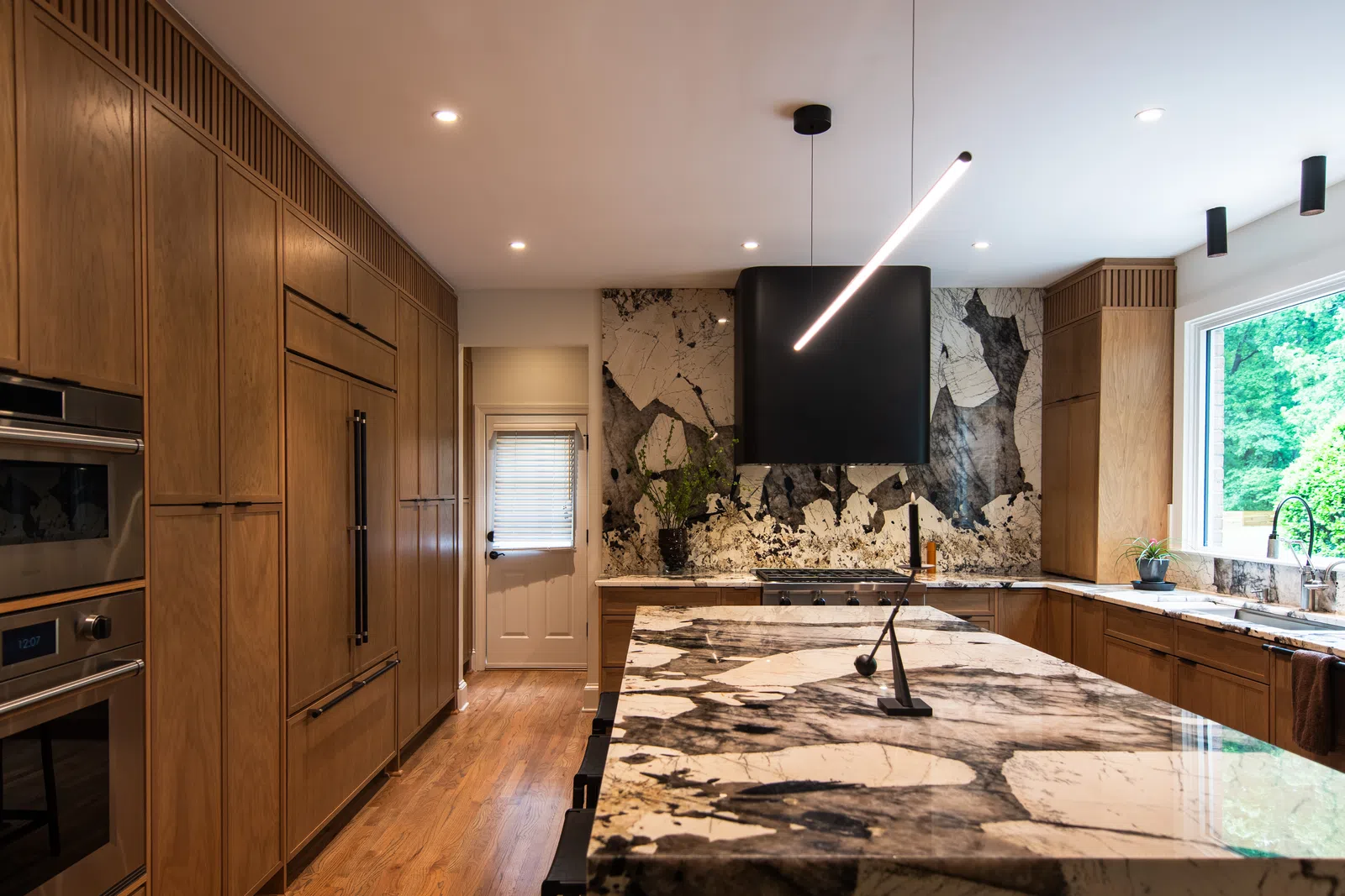 Modern kitchen with large patterned marble island, wooden cabinets, stainless steel appliances, and large window.