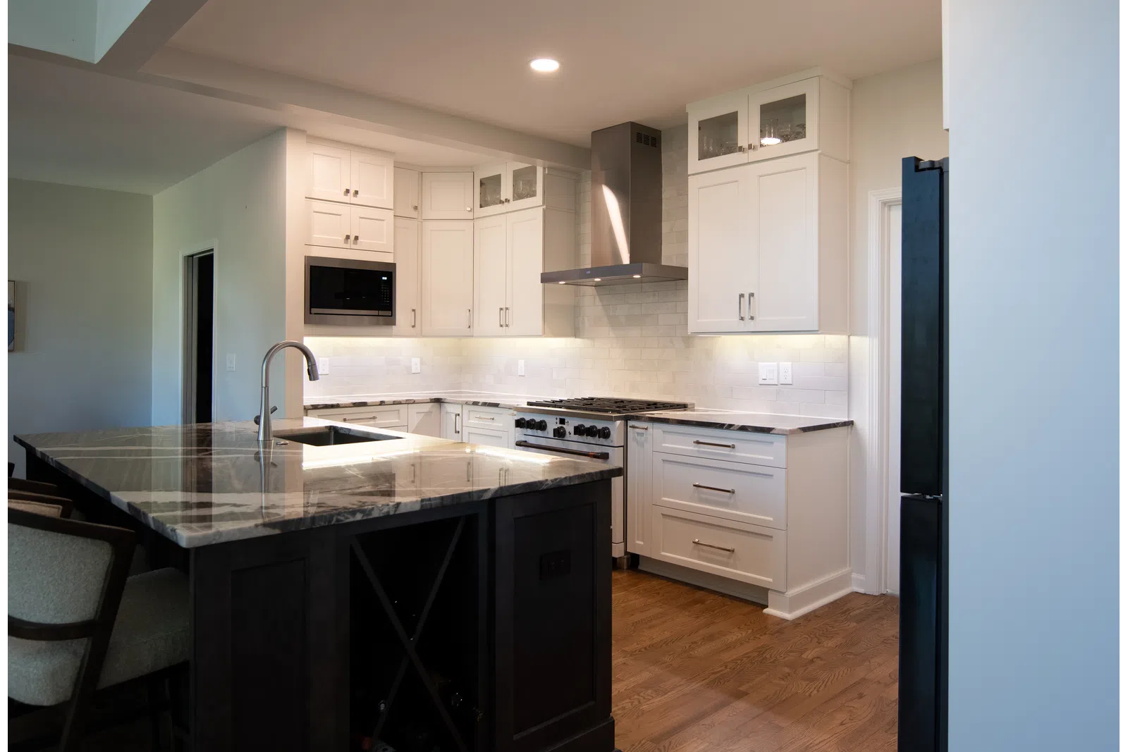 Modern kitchen with white cabinets, marble island countertop, stainless steel appliances, and hardwood floors