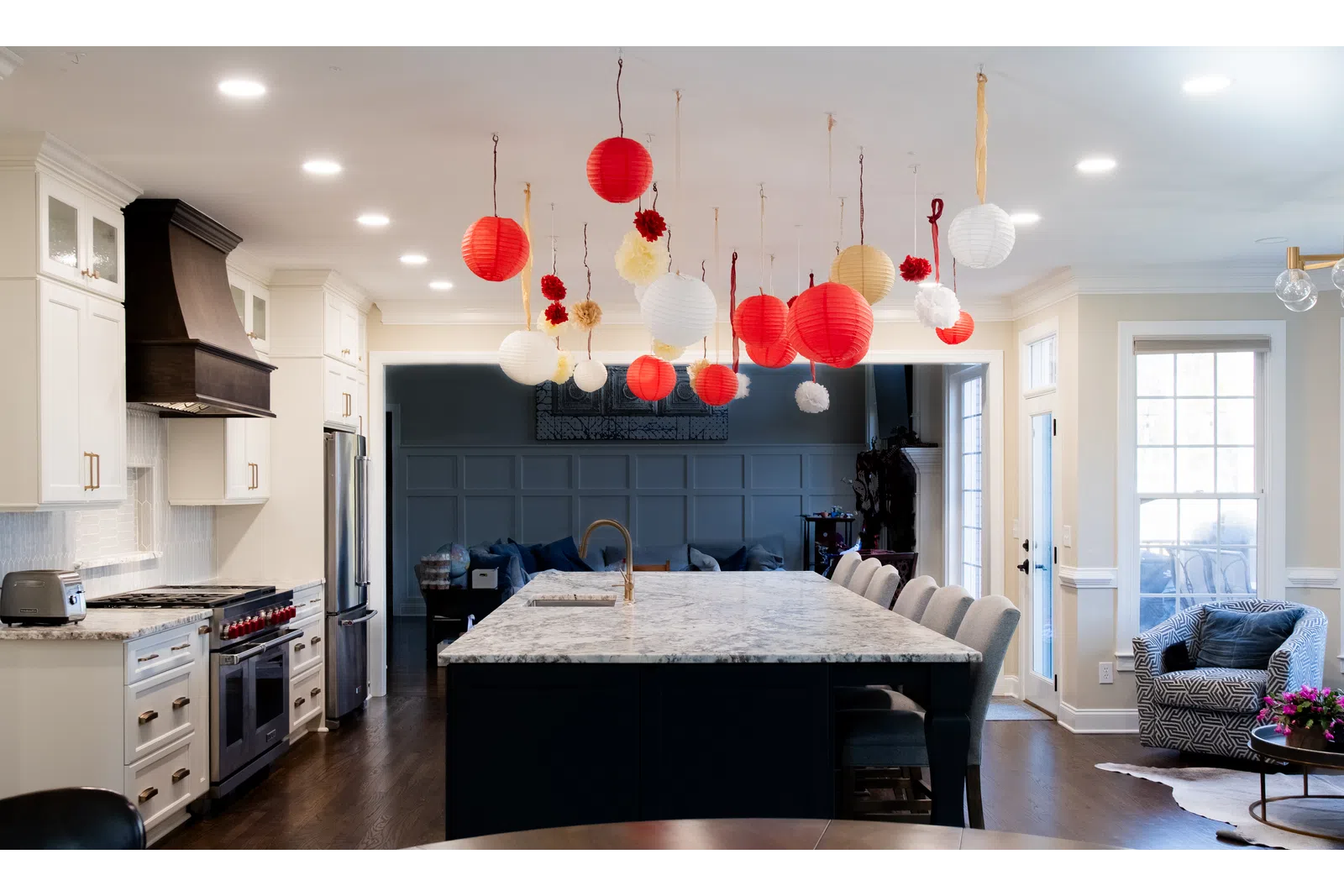 Modern kitchen with marble island, white cabinetry, stainless appliances, and red and white hanging lantern decorations.